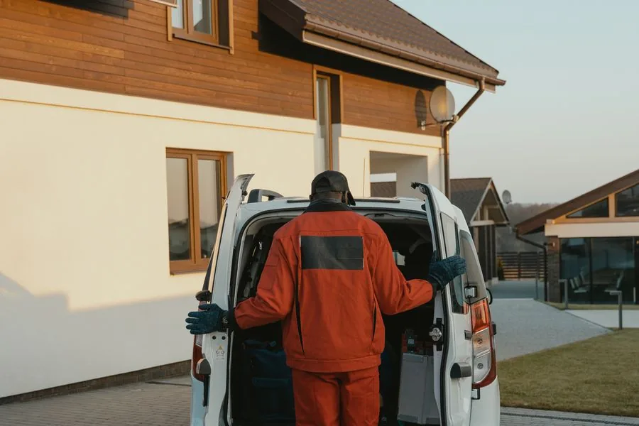 A home services technician arriving at a residential property with a service van